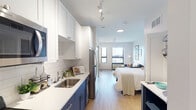 This single-floor studio unit at 2717 Fourth St SE in Minneapolis offers a well-designed open layout that efficiently combines living, sleeping, and dining functions within one cohesive space. Light-toned hardwood flooring runs throughout, lending warmth and visual continuity from the entry to the window-facing living area.

The galley-style kitchen is a standout feature, finished with two-tone cabinetry — navy blue lower cabinets paired with crisp white upper cabinets — complemented by a white subway tile backsplash and clean white countertops. Stainless steel appliances, including a refrigerator, range, microwave, and dishwasher, complete the functional kitchen setup. Track lighting overhead provides ample task illumination along the kitchen corridor.

The open main area accommodates both a sleeping space and a living area, benefiting from large windows that allow generous natural light and provide elevated views of the surrounding Minneapolis neighborhood. The bright, neutral palette of white and soft gray walls enhances the sense of openness throughout.

The bathroom is finished with large-format gray tile flooring, a navy vanity with a white countertop, and a separate shower area, maintaining the same refined two-tone design language found in the kitchen. The overall ambiance is clean, modern, and practical.