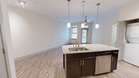 Located at 300 State St in downtown Knoxville, Tennessee, this one-bedroom, one-bathroom residence offers a thoughtfully designed open-concept layout across a single floor. The kitchen serves as a central focal point, featuring dark espresso cabinetry, granite countertops, a subway tile backsplash, and a full suite of stainless steel appliances including a French door refrigerator, electric range, and built-in microwave. A kitchen island with a double basin sink and pendant lighting above creates a seamless transition into the open living area, which features wood-style flooring and a ceiling fan. Natural light flows in through multiple windows fitted with blinds, and a glazed entry door provides access to an outdoor balcony. The bedroom is carpeted for comfort, includes a ceiling fan, a large window with outdoor views, and benefits from direct access to both a dedicated walk-in closet and the hallway. The bathroom is finished with white subway tile surrounding a full soaking tub and shower combination, complemented by tile flooring. A hallway connects all rooms efficiently, with an in-unit washer and dryer also visible. The overall aesthetic is clean and contemporary throughout.