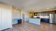 Located at Hiker Peak View in Colorado Springs, Colorado, this single-floor residence offers a contemporary design with a thoughtful, open layout. The kitchen serves as a central highlight, showcasing dark espresso-toned cabinetry that extends floor to ceiling, providing generous storage throughout. Granite countertops run along the perimeter and continue onto a central island, offering both prep space and a natural gathering point. A white subway tile backsplash adds a clean contrast to the cabinetry, while stainless steel appliances—including a French door refrigerator, electric range, and over-the-range microwave—complete the modern aesthetic. Wood-look plank flooring flows throughout the main living and kitchen areas, contributing warmth and continuity.

A built-in desk or secondary counter with matching dark cabinetry and granite is positioned adjacent to the kitchen, adding a functional workspace to the open-plan area. The bedrooms feature plush carpet flooring and ceiling fans, with windows that bring in natural light and exterior views. The bathroom includes a tub-shower combination with white tile surround and brushed nickel fixtures. A carpeted stairwell with a handrail and a narrow window connects to an entryway below, rounding out this well-appointed residence.