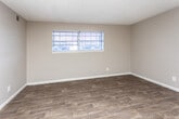 This single-floor space is designed with a practical, straightforward layout that maximizes functionality across its rooms. Throughout the unit, dark wood-look flooring provides a cohesive, modern aesthetic, complemented by neutral gray-toned walls and white baseboards. Textured ceilings add a subtle architectural detail consistent across all rooms.

The living area is open and welcoming, with direct access to the front entry door and a visual connection to the kitchen. A ceiling fan serves this main living space, enhancing comfort and airflow. The kitchen is equipped with gray cabinetry, granite-style light countertops, a black electric range with coil burners, and an overhead range hood, providing a clean and functional cooking environment.

Multiple bedrooms are present throughout the unit, each featuring the same wood-look flooring, neutral walls, and individual windows fitted with horizontal blinds that allow natural light to filter in while maintaining privacy.

The bathroom includes a full-size white soaking tub and shower combination with a tiled surround, a toilet, and wood-look tile flooring, maintaining a clean and utilitarian design. Overall, the space presents a consistent, move-in-ready aesthetic with practical finishes suited for everyday living.