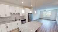 Located at 2725 South Blvd in Charlotte, NC, this single-floor residence offers a clean, modern design with an open and airy layout. The kitchen is a standout feature, showcasing white shaker-style cabinetry, granite countertops, a subway tile backsplash, and a full suite of stainless steel appliances including a refrigerator, dishwasher, range, and microwave. A center island with a contrasting base and matching granite surface provides additional prep space and casual seating. Pendant lighting above the island and recessed ceiling lights add a polished, contemporary feel throughout the kitchen. The open-concept design flows seamlessly into the living area, which benefits from natural light through large windows and features a ceiling fan, built-in shelving, and durable hardwood-style flooring. The bedroom offers plush carpeting and ample wall space, while the bathroom includes a tub-shower combination, granite-topped vanity, and access to a walk-in closet. Neutral tones and clean finishes throughout create a cohesive, move-in-ready aesthetic, making this Charlotte residence a well-appointed and functional living space.