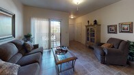 This single-floor residence offers a thoughtfully arranged layout with a warm, traditional aesthetic carried throughout each room. The living area is anchored by neutral tile flooring and features a sliding glass door that opens to a private patio, filling the space with natural light and providing easy outdoor access. The kitchen is outfitted with light wood cabinetry, a coil-top range, dishwasher, and a double-basin sink with ample counter space. A pendant light fixture illuminates the adjoining dining area, which comfortably accommodates a round glass-top table with ornate wrought iron seating. Conveniently accessed directly from the kitchen is a dedicated laundry room with a full-size washer and dryer. The primary bedroom features wood-look flooring, a ceiling fan, window with natural light, and generous space for full bedroom furnishings. A second bedroom offers tile flooring and warm ambient lighting. The two bathrooms include one with a glass-enclosed shower and soaking tub combination, and a second featuring a tub-shower combo with floor-to-ceiling tile surround and elegant curtain detailing. Throughout, the home maintains a cohesive, comfortable character with warm tones and classic finishes.