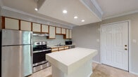 Located in Sandy Springs, GA, this single-floor residence at 7227 Peachtree Dunwoody offers a well-organized layout with comfortable living spaces throughout. The kitchen serves as a central hub, equipped with stainless steel appliances including a refrigerator, electric range, dishwasher, and microwave. Wood-trimmed cabinetry with cream-colored fronts lines the walls, providing ample storage, while a central island with a clean white countertop offers additional prep and dining space. Tile flooring runs through the kitchen, transitioning to plush carpet in the living and bedroom areas. The living area is bright and open, featuring recessed lighting, crown molding, and a sliding glass door that brings in natural light and outdoor access. The bedroom is generously sized with a ceiling fan, a large window framing natural greenery, and soft carpet underfoot. A dedicated laundry area houses a stacked washer and dryer unit, adding everyday convenience. The bathroom features tile flooring, a full tub-shower combination with classic white tile surround, and a vanity with wood-accented cabinetry. Throughout the space, a textured ceiling, crown molding, and neutral-toned walls create a cohesive and functional living environment.