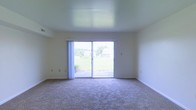 This two-floor residential space offers a clean, functional layout designed for comfortable everyday living. The main living area is a standout feature, showcasing wall-to-wall carpeting that adds warmth underfoot and a bright, open atmosphere enhanced by smooth, white ceilings. A large sliding glass door serves as the focal point of the living space, flooding the room with abundant natural light and providing direct access to an outdoor patio area. The view through the glass door reveals a well-maintained green lawn and a backdrop of mature trees, offering a pleasant and tranquil outdoor setting. The neutral-toned walls throughout create a versatile canvas, easily adaptable to a variety of interior styles. The overall design of the space is understated and practical, with clean lines and minimal architectural ornamentation that keep the focus on light and openness. Spanning two floors, the layout provides a natural separation between living and private spaces, offering both functionality and a sense of spatial variety. The space presents itself as a well-maintained, move-in ready environment suited to those seeking a straightforward, comfortable place to call home.