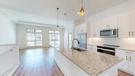 Located at 4271 Woodward Mill Rd in Buford, GA, this two-story home offers a well-designed layout with modern finishes throughout. The open-concept kitchen serves as the heart of the main living area, featuring an expansive granite island with an undermount sink, crisp white shaker cabinetry, a decorative tile backsplash, stainless steel appliances, and stylish pendant lighting. The kitchen flows seamlessly into the living area, which is bathed in natural light from large windows with transom accents and light hardwood-style flooring underfoot. An additional room on the main floor features tray ceilings and large windows offering outdoor views, providing a bright and airy atmosphere. Upstairs, carpeted bedrooms offer a comfortable retreat, including a spacious room with dual windows and a generous walk-in closet outfitted with wire shelving. The bathroom includes a soaking tub surrounded by elegant marble-look tile. A dedicated laundry area houses a full-size washer and dryer. The attached two-car garage provides ample parking and storage space, complete with an automatic opener. Carpeted stairs with a white handrail connect the two levels, completing this thoughtfully appointed home.