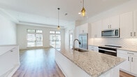 Located at 4271 Woodward Mill Rd in Buford, GA, this two-story home offers a well-designed layout with modern finishes throughout. The open-concept kitchen serves as the heart of the main living area, featuring an expansive granite island with an undermount sink, crisp white shaker cabinetry, a decorative tile backsplash, stainless steel appliances, and stylish pendant lighting. The kitchen flows seamlessly into the living area, which is bathed in natural light from large windows with transom accents and light hardwood-style flooring underfoot. An additional room on the main floor features tray ceilings and large windows offering outdoor views, providing a bright and airy atmosphere. Upstairs, carpeted bedrooms offer a comfortable retreat, including a spacious room with dual windows and a generous walk-in closet outfitted with wire shelving. The bathroom includes a soaking tub surrounded by elegant marble-look tile. A dedicated laundry area houses a full-size washer and dryer. The attached two-car garage provides ample parking and storage space, complete with an automatic opener. Carpeted stairs with a white handrail connect the two levels, completing this thoughtfully appointed home.