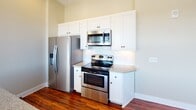 Located at 450 Hay St in downtown Fayetteville, NC, this single-floor unit offers a thoughtfully designed layout with a clean, contemporary aesthetic. The open-concept living and dining area is anchored by rich, dark hardwood flooring that extends throughout the main living spaces, creating a warm and inviting atmosphere. Generous windows dressed with white blinds flood the area with natural light while offering views of the surrounding cityscape.

The kitchen is a standout feature, equipped with stainless steel appliances including a refrigerator, electric range, and over-the-range microwave. White shaker-style cabinetry reaches to the ceiling for ample storage, while granite countertops and a classic subway tile backsplash add a polished finish. A kitchen island with a built-in sink and pendant lighting above provides both functionality and style.

The bedrooms are carpeted for comfort and each includes a ceiling fan and a window with outdoor views, offering a quiet retreat. Two full bathrooms serve the unit, both featuring marble-style tile flooring, white vanities, and clean, neutral finishes. One bathroom includes a shower/tub combination with tiled surround. The overall design is neutral and move-in ready, well-suited for comfortable urban living in the heart of Fayetteville.