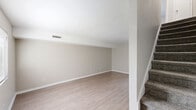 This two-story townhome in Lincolnton, North Carolina offers a practical and well-organized layout across two floors. The main level features a bright living room finished with light luxury vinyl plank flooring that extends throughout the common areas, creating a cohesive and easy-to-maintain space. A window allows natural light to filter in, adding warmth to the open feel. The kitchen is equipped with stainless steel appliances — including a refrigerator, range, and dishwasher — complemented by crisp white cabinetry and matching light flooring. A convenient half bathroom on the main floor completes the first level. A staircase connects to the upper floor, where both bedrooms are located. The generously sized primary bedroom offers plush carpeting and ample space for furnishings, while the second bedroom also features carpet flooring and a window with outdoor views. Each upstairs bedroom is served by its own bathroom, with one featuring a white vanity with a large mirror and bright lighting. The bathrooms are finished in neutral tones with light wood-style flooring. Throughout the home, a consistent neutral color palette of soft beiges and whites creates a clean, move-in ready atmosphere well suited for comfortable everyday living.