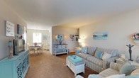 Located at 835 Blooming Grove Turnpike in New Windsor, New York, this single-floor residence offers a comfortable and thoughtfully arranged living environment. The open layout connects the living room and dining area in a seamless flow, creating a sense of spaciousness throughout. The living room features warm carpeted flooring, neutral-toned walls, and ample space for relaxed seating arrangements, as evidenced by the striped sofa and coordinating furnishings that lend a light, coastal-inspired ambiance. Soft, layered lighting from wall sconces and table lamps enhances the inviting atmosphere. Adjacent to the living room, the dining area benefits from natural light streaming through a window, complemented by an elegant chandelier overhead, making it an ideal space for both everyday meals and entertaining. The overall color palette throughout the space is calm and neutral, with soft blues and whites accenting the décor to create a bright, airy feel. The single-floor design ensures easy accessibility and a cohesive flow from room to room. Situated in New Windsor, NY, the property is positioned within a well-established community in the Hudson Valley region, offering convenient access to local amenities and transportation routes.