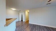 This single-floor unit is designed with a clean, modern aesthetic throughout. The open living area is anchored by wood-style plank flooring in a warm gray tone, complemented by soft neutral wall colors and white baseboards. A ceiling fan with a light fixture provides both comfort and illumination, while vertical blinds on the windows allow natural light to filter in with views of outdoor greenery.

The kitchen features white shaker-style cabinetry, granite-look countertops, and black appliances including a range, refrigerator, and dishwasher. A peninsula with a sink separates the kitchen from the living area, offering a functional and open layout.

The bedrooms are generously sized, each equipped with ceiling fans and windows that invite natural light. Sliding-door closets with built-in wire shelving provide practical storage solutions.

The bathrooms are finished with large-format marble-style ceramic tile flooring and tiled shower surrounds. One bathroom includes accessibility features such as grab bars, indicating thoughtful, inclusive design. Additional storage is accessible via a walk-in closet with wire shelving adjacent to one of the bathrooms.

Overall, the space presents a bright, functional, and cohesive living environment.
