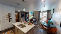 Located at 6811 E Main St in the heart of Scottsdale, Arizona, this single-floor residence offers a thoughtfully designed layout with a distinct mid-century modern flair. The open-concept kitchen is a standout feature, boasting quartz countertops, a large kitchen island with a deep stainless steel sink, stainless steel appliances including a French door refrigerator and gas range, white cabinetry with sleek hardware, a tile backsplash, and pendant lighting overhead. Dark hardwood floors flow seamlessly into the living area, where a vibrant teal sofa, eclectic sunburst wall décor, a ceiling fan, and a sliding glass door leading to a private outdoor balcony create an inviting and lively atmosphere. The balcony overlooks a landscaped outdoor area with palm trees, allowing natural light to fill the room. The bedroom is a serene retreat, featuring plush carpet, sheer draping curtains, a ceiling fan, a statement metallic headboard wall, and ample natural light from large windows. The bathroom is well-appointed with a tub-shower combination, quartz vanity countertop, and tasteful decorative accents. Throughout the space, bold artwork and curated furnishings contribute to a cohesive, vibrant, and welcoming ambiance.