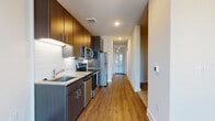 This single-floor unit showcases a cohesive modern design with warm hardwood-style flooring running throughout the space. The kitchen is a standout feature, equipped with a full suite of stainless steel appliances, including a range, microwave, dishwasher, and refrigerator. Rich dark-toned cabinetry extends from floor to ceiling, complemented by granite countertops, an undermount sink, and a clean white subway tile backsplash with under-cabinet lighting. The layout connects the kitchen seamlessly to the open living area, which benefits from large sliding glass doors that invite abundant natural light and provide outdoor access. The bedroom is a well-proportioned, quiet space with a window fitted with blinds for light control and a ceiling fan for added comfort. The bathroom maintains the same design language found throughout the unit, featuring dark cabinetry, granite countertops, an undermount sink, and hardwood-style flooring. Recessed lighting and crisp white walls create a bright, clean ambiance across all areas, while the thoughtful floor plan, visible in the 3D overview, offers an efficient and functional flow between spaces.