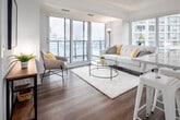 Located at 20 Samuel Wood Way in Toronto, this single-floor suite presents a clean, contemporary design characterized by crisp white walls, warm wood-tone flooring, and recessed lighting throughout. The open-concept layout connects the kitchen and living areas seamlessly, creating a functional and visually cohesive space.

The kitchen is outfitted with sleek, flat-front white cabinetry extending to the ceiling, stainless steel appliances including a refrigerator, electric range, and built-in microwave, as well as a large island with an undermount sink and ample counter space. Track lighting overhead highlights the modern, minimalist aesthetic.

The living area is bright and airy, anchored by expansive floor-to-ceiling windows and a sliding glass door leading to a private balcony with open city views of the Toronto skyline. Natural light fills the space generously, enhancing its welcoming ambiance.

The bedrooms are well-proportioned with wood-tone flooring, built-in double closets, and a calm, neutral palette. Two bathrooms serve the suite — one features a glass-enclosed walk-in shower with tile surround, while the second includes a tub-shower combination with chrome fixtures and a glass shelf. Both are finished with white countertops and modern hardware.

A hallway connects all areas efficiently, with a full-length mirror adding depth to the entry corridor.