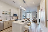 Located in Matthews, NC, this thoughtfully designed one-bedroom, two-bathroom residence offers a seamless open-concept layout that maximizes every square foot. The combined kitchen and living area serves as the heart of the home, anchored by a large center island with quartz countertops and seating for multiple guests, illuminated by a striking rectangular pendant light fixture. The kitchen features two-tone cabinetry in white and natural wood, subway tile backsplash, stainless steel appliances including a side-by-side refrigerator, and a built-in wine rack — all flowing effortlessly onto light-toned hardwood-style flooring. The living room is bright and airy, benefiting from large windows and French doors that open to a private patio, with a ceiling fan adding comfort overhead. The primary bedroom is generously sized, featuring large windows that invite abundant natural light, plush carpeting, and access to a spacious walk-in closet with wrap-around wire shelving. The primary bathroom is elegantly appointed with dual vanities, wood-toned cabinetry, hardwood-style flooring, and a tiled soaking tub. A laundry area and utility room add everyday practicality to this well-appointed residence.