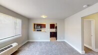 This single-floor residential unit offers a practical and comfortable layout designed for everyday living. The open living and dining area is finished with plush gray carpeting and neutral gray walls, creating a clean, inviting atmosphere. A distinctive pass-through window connects the living area directly to the kitchen, providing both visual openness and functional convenience.

The kitchen is equipped with rich dark mahogany cabinetry featuring brushed nickel hardware, light granite-style countertops, a stainless steel single-basin sink, and black appliances including a refrigerator, dishwasher, and microwave. Tile flooring and ample upper and lower cabinet storage make this a highly functional cooking space.

Two carpeted bedrooms offer comfortable retreats, each featuring wall-unit HVAC systems for individual climate control and windows with blinds that allow natural light to fill the rooms. At least one bedroom includes a closet with bifold doors, providing useful storage space.

The bathroom is cleanly finished with a white tub-shower combination, a built-in shower niche, and a window that brings in natural light. Throughout the unit, clean white trim and baseboards complement the neutral palette, contributing to a bright and cohesive aesthetic that is move-in ready.