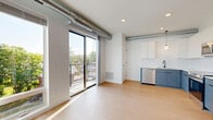 Located at 304 N Second St in Mankato, MN, this 1-bedroom, 1-bathroom unit offers a thoughtfully designed open-concept layout with contemporary finishes throughout. Light-toned hardwood-style flooring runs continuously across the entire space, enhancing the bright, clean aesthetic.

The open living and kitchen area is a standout feature, highlighted by exposed industrial-style ductwork along the ceiling, recessed lighting, and a large sliding glass door that opens to a private balcony with outdoor views of the surrounding neighborhood. The kitchen is well-appointed with two-tone cabinetry — slate-blue lower cabinets paired with white uppers — white countertops, a stainless steel refrigerator, range, microwave, and dishwasher, along with a globe pendant light that adds a modern touch.

The bedroom is a well-proportioned, private retreat with recessed lighting and its own dedicated closet equipped with wire shelving for organized storage. The bathroom features a clean, minimalist design with a white vanity, matte black fixtures, and a large mirror. A dedicated in-unit laundry area with a stacked washer and dryer provides added convenience. A bright hallway connects all rooms, completing this efficiently designed and move-in ready unit.