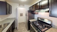 This premium single-floor residence features three bedrooms and two bathrooms within a thoughtfully designed layout. The kitchen is equipped with stainless steel appliances, including a gas range and refrigerator, complemented by rich dark cabinetry and granite-style countertops. Wood-look flooring runs through the kitchen and utility areas, adding a clean, modern touch.

The open living area is generously sized, anchored by a granite-topped breakfast bar that connects seamlessly to the kitchen. A large window fills the space with natural light and offers views of the surrounding greenery. The carpeted living area flows directly into the hallway leading to the bedrooms.

Each bedroom features plush carpet flooring and a dedicated closet for ample storage. One bedroom enjoys a bright window with outdoor views, while the primary bedroom provides direct access to an en-suite bathroom. Both bathrooms are well-appointed with granite vanity tops, dark cabinetry, tiled shower-tub combos, and wood-look flooring.

A utility closet with an electrical panel is conveniently located off the kitchen. Throughout the home, neutral walls, consistent finishes, and a clean, open feel create a comfortable and functional living environment suited for everyday living.