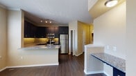 Located within The Coves community in Saint Petersburg, Florida, this single-story residence offers a well-designed layout with consistent, contemporary finishes throughout. Dark hardwood-style flooring runs through the main living and kitchen areas, providing a cohesive foundation for the space.

The kitchen serves as a central highlight, outfitted with dark espresso cabinetry extending to the ceiling for generous storage, granite countertops, a subway tile backsplash, and stainless steel appliances including a refrigerator, range, and microwave. A multi-level kitchen island with matching granite offers additional prep and seating space, while track lighting overhead ensures ample illumination. A secondary counter ledge adjacent to the kitchen provides additional functional workspace.

A hallway connects the main living area to the private rooms, where plush carpet flooring transitions from the hardwood. The bedroom features a walk-in closet with built-in shelving, providing organized storage. An additional closet is also accessible from the bedroom corridor.

The bathroom includes dark vanity cabinetry with granite countertops, a tub-shower combination, and hardwood-style flooring that mirrors the main living areas. Warm neutral wall tones are carried throughout the unit, lending a unified, welcoming ambiance to the overall space.