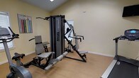 This dedicated fitness room offers a focused and functional workout environment housed within a single-floor facility. The space is outfitted with a professional-grade Precor multi-station strength training machine, a well-recognized brand in the fitness industry known for its durability and versatility. The equipment includes multiple workout stations, accommodating exercises such as leg presses, lat pulldowns, and various upper-body movements, making it suitable for a full-body strength training routine.

The room features neutral, light yellow walls and carpeted flooring, contributing to a clean and comfortable atmosphere. A window with horizontal blinds allows for natural light to filter into the space, keeping the environment bright without harsh glare. The ceiling is smooth and well-lit, ensuring clear visibility throughout the room.

The layout is efficiently organized, with the equipment positioned to allow adequate space for movement and safe use of each station. The overall ambiance is practical and purpose-driven, catering to users who prioritize structured strength training. Whether used as a private gym or a shared amenity fitness room, this space delivers a comprehensive workout setting with quality equipment in a tidy, well-maintained environment.