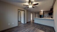 Located at 1435 W Talmage St in Springfield, Missouri, this single-floor unit offers a cohesive, modern aesthetic throughout. Dark hardwood-style flooring runs continuously across the living areas, creating a unified and contemporary feel.

The open living area is anchored by a ceiling fan with integrated lighting and connects seamlessly to the kitchen via a peninsula-style counter with a light stone surface, ideal for casual dining or meal prep. The kitchen is well-appointed with wood-toned lower and upper cabinetry, open shelving with decorative tile backsplash, and a full suite of black appliances including a refrigerator, range, microwave, and ample counter space.

The bedroom is a comfortably sized, private room outfitted with a ceiling fan and access to an adjacent laundry area with washer and dryer hookups, adding significant convenience.

The bathroom features a dark wood vanity with a marble-style countertop, a large mirror with overhead lighting, and a full-size soaking tub and shower combination with clean white surrounds and hardwood-style flooring extending throughout.

Neutral gray walls and dark trim accents tie the space together, lending a clean, modern sensibility throughout. The layout is efficient and well-organized, making this unit a practical and stylish option in Springfield, MO.