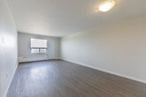 Located on the 14th floor at 940 Commissioners Rd in London, Ontario, this one-bedroom, one-bathroom unit offers a clean, modern aesthetic with a practical and efficient layout. The living room is a bright, open space featuring light grey laminate flooring, neutral white walls, and a large window that frames expansive city views — flooding the room with natural light and offering a connection to the London skyline. A baseboard heating unit runs beneath the window, ensuring year-round comfort. The bedroom continues the same laminate flooring and neutral palette, with its own window providing additional natural light and elevated views of the surrounding cityscape. The kitchen is compact and functional, featuring dark granite-style countertops, white cabinetry, and a white electric range — offering everything needed for day-to-day meal preparation. The bathroom is well-appointed with a full tub-shower combo, a white vanity topped with a dark granite-style counter, a large mirror with overhead lighting, and tile flooring. Throughout the unit, the consistently neutral tones and clean finishes create a calm, move-in-ready atmosphere suited for comfortable urban living.
