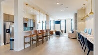Located at 6160 Hall Rd in Galloway, Ohio, this well-appointed single-story community space offers a thoughtfully designed layout across a generously sized floor plan. The welcoming entrance foyer features soaring ceilings, light tile flooring, and structural columns that frame the open-concept interior, setting an inviting tone from the moment you arrive.

The combined kitchen and living area serves as the heart of the space. The kitchen is outfitted with warm wood cabinetry, a striking blue tile backsplash, stainless steel appliances, and a white quartz peninsula bar topped with leather-seated barstools and illuminated by a row of elegant brass pendant lights. The adjacent living area features a floor-to-ceiling whitewashed brick fireplace, large windows dressed in bold patterned drapery, and a wall-mounted television, creating a comfortable and visually dynamic gathering space.

The dedicated media room offers a more intimate retreat, complete with a large wall-mounted screen, plush neutral seating, warm leather accent chairs, and ample natural light from oversized windows with plaid curtains. A popcorn machine adds a fun, cinematic touch.

Throughout, the space maintains a cohesive aesthetic of neutral tones accented by blue textiles, brass fixtures, and tile flooring, resulting in an atmosphere that is both stylish and functional for community gatherings.