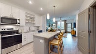 Located at 8050 Lapis Ln NW in Concord, North Carolina, this well-appointed single-floor residence combines modern design with comfortable, functional living. The open-concept layout seamlessly connects the kitchen and living area, creating an inviting and cohesive space throughout.

The kitchen is a standout feature, outfitted with crisp white cabinetry, gray lower cabinets, granite countertops, a white subway tile backsplash, and a full suite of stainless steel appliances including a refrigerator, range, and microwave. A spacious center island with bar seating and pendant lighting serves as a natural gathering point. Light wood-style flooring flows throughout the main living areas, enhancing the bright, airy atmosphere.

The living room is anchored by a soothing teal accent wall, a ceiling fan, and large windows with access to an outdoor balcony, filling the room with natural light. The bedroom continues the teal accent wall motif and features a generous window that brings in additional daylight. The bathroom is finished with large-format tile flooring, a granite-topped gray vanity with brushed nickel hardware, and a tub-shower combination. A dedicated in-unit laundry closet with shelving above provides added convenience. This residence offers a cohesive, contemporary aesthetic throughout.
