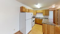 Located at 2551 Villa Dr S in Fargo, North Dakota, this single-floor unit offers a practical and well-organized layout with a clear separation between living, sleeping, and functional areas. The kitchen is a standout feature, equipped with warm honey-toned oak cabinetry, granite-style laminate countertops, a peninsula for added prep space, and white appliances including a refrigerator, electric range, built-in microwave, and a double-basin sink. Light hardwood-style flooring extends throughout the kitchen and entry area, contributing to a bright and cohesive feel. The open living area transitions from the kitchen and features a ceiling fan, a textured ceiling, and a sliding glass door dressed with vertical blinds that allows for natural light. Baseboard heating is present throughout the unit. The bedroom is generously sized with plush carpeting, a window with vertical blinds, and ample wall space. A mirrored closet is visible near the entry. The bathroom is finished with light ceramic tile flooring, a full tub and shower combination with white tile surround, a toilet, and oak vanity cabinetry. Overall, the space presents a clean, functional design well-suited for comfortable everyday living.