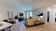 This thoughtfully designed single-floor residence offers a cohesive blend of modern aesthetics and functional living spaces. The open-concept living room serves as the heart of the home, featuring light wood-style flooring, recessed lighting, and a large window with access to a balcony that invites natural light into the space. A spacious sectional sofa, media console, and curated artwork create a warm yet contemporary atmosphere.

Adjacent to the living area, the dining space is defined by track lighting overhead and features a wooden dining table with seating for four. A striking gold-framed artwork anchors the wall, adding a bold artistic focal point to the room.

The kitchen is well-equipped with stainless steel appliances, including a side-by-side refrigerator, gas range, built-in microwave, and oven. Dark lower cabinetry is contrasted by bright white upper cabinets, while granite countertops and light wood flooring complete the polished look.

Both bedrooms are comfortably scaled with ceiling fans, neutral carpeting, and soft, muted tones that promote a restful environment. The primary bedroom includes a walk-in closet, offering generous storage. The bathroom is finished with a granite-topped dark vanity, a large framed mirror, and a glass-enclosed walk-in shower, all set against clean white walls and light wood flooring.