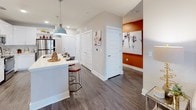 This single-story, two-bedroom, two-bathroom residence combines contemporary design with functional living. The kitchen is a standout feature, outfitted with crisp white cabinetry, quartz countertops, stainless steel appliances including a refrigerator, electric range, and microwave, as well as a tile backsplash and a pendant-lit island with bar seating. Wood-style flooring runs through the kitchen and main living areas, lending a cohesive, modern aesthetic. The living room offers a comfortable layout with natural light streaming through large windows dressed with stylish drapes.

Both bedrooms are carpeted and well-proportioned, each featuring ceiling fans and windows that bring in natural light. The primary bedroom connects to an en-suite bathroom and a walk-in closet finished with bold accent walls and built-in shelving. The primary bathroom features white cabinetry, granite countertops, an undermount sink, and wood-style flooring. The second bathroom mirrors this design with a granite-topped vanity, large mirror, and a shower-tub combination. Throughout the residence, neutral gray walls provide a versatile backdrop, accented by warm terracotta tones in select areas, creating a balanced and inviting ambiance.