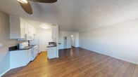 Located at 6455 Reseda Blvd in the Reseda neighborhood of Los Angeles, this single-floor unit offers a functional and well-organized layout. The open-concept living and dining area is finished with rich, dark hardwood-style flooring that extends throughout the main living space, creating a warm and cohesive feel. A ceiling fan anchors the living room, which is filled with natural light from multiple windows. A wall-mounted HVAC unit provides climate control.

The galley-style kitchen is efficiently designed with white cabinetry both above and below dark countertops, a stainless steel sink with a modern faucet, a gas range, a built-in microwave, and a full-size refrigerator. Light wood-tone flooring in the kitchen complements the overall aesthetic.

The bedroom is carpeted and generously sized, featuring a large window with views of mature trees outside, offering a sense of privacy and greenery. A mirrored sliding-door closet provides substantial storage space.

The bathroom is accessed via a hallway and includes a white vanity with dark countertop, a medicine cabinet mirror, and a separate room housing a full soaking tub with white tile surround. The textured ceilings throughout the unit are a consistent architectural detail tying the spaces together.