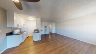 Located at 6455 Reseda Blvd in the Reseda neighborhood of Los Angeles, this single-floor unit offers a functional and well-organized layout. The open-concept living and dining area is finished with rich, dark hardwood-style flooring that extends throughout the main living space, creating a warm and cohesive feel. A ceiling fan anchors the living room, which is filled with natural light from multiple windows. A wall-mounted HVAC unit provides climate control.

The galley-style kitchen is efficiently designed with white cabinetry both above and below dark countertops, a stainless steel sink with a modern faucet, a gas range, a built-in microwave, and a full-size refrigerator. Light wood-tone flooring in the kitchen complements the overall aesthetic.

The bedroom is carpeted and generously sized, featuring a large window with views of mature trees outside, offering a sense of privacy and greenery. A mirrored sliding-door closet provides substantial storage space.

The bathroom is accessed via a hallway and includes a white vanity with dark countertop, a medicine cabinet mirror, and a separate room housing a full soaking tub with white tile surround. The textured ceilings throughout the unit are a consistent architectural detail tying the spaces together.