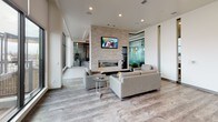 The High Pointe Lobby presents a sophisticated and contemporary design that immediately sets a refined tone upon entry. The main entrance features floor-to-ceiling glass doors and windows beneath a striking wood-paneled ceiling, flooding the space with natural light and offering clear sightlines to the exterior. A branded entry mat anchors the welcoming foyer, which opens into a spacious lounge area.

The centerpiece of the lounge is a floor-to-ceiling stacked stone fireplace wall, complete with a linear gas fireplace and a wall-mounted television above. Comfortable upholstered seating arrangements with glass-topped coffee tables create an inviting atmosphere for residents and guests. Large windows along the perimeter further enhance the sense of openness.

A standout feature is the rich wood accent wall — dressed in warm vertical planking beneath a matching wood ceiling — flanked by glass-partitioned rooms and accented with potted greenery, adding a natural, textural contrast to the otherwise light and neutral palette.

The lobby also includes a fully appointed kitchen with rich dark cabinetry, granite countertops, a mosaic tile backsplash, stainless steel appliances, and a large island with bar seating illuminated by geometric pendant lights. Practical amenities such as a stainless steel elevator, parcel storage, and a luggage cart round out this well-equipped and thoughtfully designed lobby.