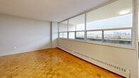 This 3-bedroom, 1-bathroom unit is thoughtfully laid out across a single floor, offering a practical and comfortable living environment. Warm parquet flooring flows consistently throughout the living areas and bedrooms, adding a classic character to the space.

The living room is a generous, light-filled area highlighted by a wide floor-to-ceiling window wall that frames sweeping city views and allows abundant natural light to pour in. It connects conveniently to the kitchen, which features grey cabinetry, granite-effect countertops, a white tile backsplash, and white appliances including a refrigerator and electric range — all finished with tile flooring.

The primary bedroom is a well-proportioned room featuring a large window with city views, parquet flooring, and access to a dedicated closet with built-in shelving. The two additional bedrooms are compact yet functional, each equipped with their own closets and the same warm parquet flooring. A central hallway connects the bedrooms efficiently, with two closets providing additional storage.

The bathroom is clean and simply appointed, featuring a full tub-shower combination with white tile surround. The unit's neutral white walls throughout create a bright, versatile backdrop ready for personalization.