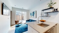Located at 10 Commerce Dr in New Rochelle, NY, this modern single-floor unit offers a thoughtfully designed open-concept layout that seamlessly connects the kitchen and living area. The kitchen is equipped with stainless steel appliances, including a gas range, built-in microwave, and full-size refrigerator, complemented by dark cabinetry, a white peninsula with a deep undermount sink, and open wall-mounted shelving. Light wood-style flooring runs throughout, adding warmth to the clean, contemporary aesthetic.

The living area is bright and inviting, benefiting from natural light that pours in through large sliding glass doors, which open onto a private outdoor space enclosed by horizontal wood slat fencing. The white walls and recessed lighting contribute to an airy, open ambiance.

The bedroom is a calm and comfortable retreat, featuring light wood flooring, crisp white walls, and ample natural light from a high window. A well-appointed full bathroom includes large-format tile flooring, a single vanity with dark cabinetry, a large mirror, and a shower/tub combination — all finished in a clean, neutral palette. This unit combines modern design with functional living in a prime New Rochelle location.