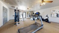 Located at 800 SW 19th St in Moore, Oklahoma, this fitness center offers a well-organized and fully equipped workout space designed to support a wide range of exercise routines. The single-floor layout provides a comfortable and functional environment for residents or members seeking convenient access to fitness amenities.

The room is finished with durable, wall-to-wall carpeting and neutral-toned walls that create a clean, focused atmosphere. Recessed lighting and ceiling fans with light fixtures are distributed throughout, ensuring the space stays well-lit and properly ventilated during workouts.

A large wall of mirrors along one side of the room enhances the sense of openness while allowing users to monitor their form. Multiple windows fitted with blinds admit generous natural light, and a set of glass double doors provides additional brightness and easy access to the exterior.

The fitness center is stocked with a robust selection of equipment, including TRUE-brand treadmills, elliptical trainers, stair climbers, and a recumbent exercise bike for cardiovascular conditioning. A multi-station cable and weight machine supports full-body strength training, and a dedicated dumbbell rack rounds out the free weight offerings. A wall-mounted television adds an entertainment option for those logging longer cardio sessions. The space is thoughtfully arranged to allow users to move freely between stations.