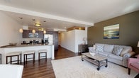 Located in the heart of downtown Madison, Wisconsin, this modern residence at 316 W Dayton St offers a well-designed, open-concept floor plan that seamlessly connects the living, dining, and kitchen areas. Rich hardwood-style flooring flows throughout the main living spaces, anchoring the contemporary aesthetic.

The kitchen is thoughtfully outfitted with dark espresso cabinetry, stainless steel appliances including a full-size refrigerator, electric range, and built-in microwave, complemented by a sleek peninsula with bar seating and pendant lighting above. The living area is bright and inviting, with floor-to-ceiling windows and a sliding glass door that opens onto a private balcony, offering views of the surrounding cityscape and filling the space with natural light.

The dining area sits adjacent to the living room, benefiting from the same expansive windows. Two bedrooms provide comfortable retreats; one features an exposed concrete accent column and a high clerestory window, while the second is serene and softly lit. The bathroom is finished with tile flooring, a dark-vanity with an undermount sink, and a tiled walk-in shower. This residence combines modern finishes with a functional layout in a prime downtown Madison location.