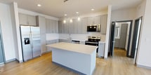 This 1,080-square-foot single-floor apartment offers 2 bedrooms, 2 bathrooms, and 3 closets, designed with a clean, contemporary aesthetic throughout. Light hardwood-style flooring runs consistently across all rooms, complemented by neutral white and gray tones that create a bright, cohesive atmosphere.

The kitchen is a standout feature, showcasing gray shaker-style cabinetry extending to the ceiling, white quartz countertops, a central island with pendant lighting, and a full suite of stainless steel Whirlpool appliances including a refrigerator with ice maker, range, microwave, and dishwasher. The adjacent living room receives abundant natural light through sliding glass doors that open onto a private balcony, offering open views of the surrounding development and beyond.

Both bedrooms are well-proportioned and feature large windows that bring in natural light. The primary bedroom measures 150 square feet and is served by its own bathroom and walk-in closet with wire shelving. The second bedroom is similarly appointed with generous window placement. Each bathroom includes a white vanity with quartz countertop, a large mirror, and hardwood-style flooring. The walk-in closets throughout the unit provide ample storage with built-in shelving systems.