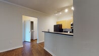 This single-floor unit offers a cohesive and functional layout highlighted by rich, dark hardwood-style flooring that runs throughout the entire space. Crown molding adds a refined architectural touch to the main living areas, complementing the neutral wall tones that create a clean, inviting atmosphere.

The open kitchen is well-appointed with light maple cabinetry, dark countertops, and a full suite of appliances including a black refrigerator, electric range, and stainless steel over-the-range microwave. Track lighting overhead ensures excellent task illumination, while a peninsula counter provides a natural divide between the kitchen and the adjacent living area.

The living room is generously proportioned, featuring a ceiling fan and direct access to a private balcony through glass-paned French doors, allowing natural light to fill the space and offering outdoor views. A separate bedroom provides a quiet retreat, with a large window that frames additional natural light and greenery beyond.

The bathroom is neatly designed with a wood-toned vanity, dark countertop, a large mirror with overhead lighting, and a full tub-shower combination framed in white tile. Accessibility-friendly grab bars are also present throughout the bathroom. An in-unit laundry area adds everyday convenience to this practical and well-designed space.