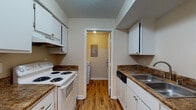 Located at 735 Marlan Ave in Reynoldsburg, Ohio, this single-floor residence offers a well-organized and functional layout designed for comfortable everyday living. The galley-style kitchen is efficiently arranged with white cabinetry lining both sides, dark laminate countertops, wood-look vinyl flooring, and white appliances including a range and refrigerator. The kitchen connects directly to a dedicated laundry room, which houses a full-size washer and dryer set and features an electrical panel for added convenience. The spacious living area is carpeted and filled with natural light through a large sliding glass door fitted with vertical blinds, providing direct access to an outdoor patio with views of surrounding greenery. The front entryway opens into this same living space, creating an inviting and open feel. The bedrooms are generously sized, each featuring plush carpeting and large windows dressed with horizontal blinds that allow ample natural light. The full bathroom is clean and well-appointed, featuring a tiled tub-shower combination, a white vanity with an integrated sink, a large mirror, and wood-look vinyl flooring. Textured ceilings are present throughout the unit, adding a classic residential character to the space.
