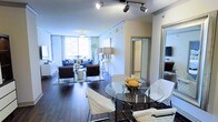 Located in Dallas, TX, this modern single-floor residence showcases a thoughtfully designed open-concept layout that seamlessly connects the living, dining, and surrounding areas. Rich, dark hardwood flooring extends throughout the space, providing a striking contrast against the bright, neutral walls and creating a warm yet sophisticated ambiance.

The living area is generously proportioned, featuring large floor-to-ceiling windows dressed with patterned curtains that flood the space with natural light. A stylish seating arrangement—including a navy blue sofa and rich brown accent chairs—anchors the room, while track lighting overhead adds a contemporary, urban edge.

Adjacent to the living area, the dining space is anchored by a round glass-top table with sleek chrome accents, surrounded by modern white upholstered chairs—an elegant setup ideal for entertaining. The open sightlines between these areas enhance the sense of spaciousness throughout.

Mirrored elements and glass accents are incorporated throughout the space, amplifying light and adding depth. A glimpse into the adjoining rooms suggests well-appointed interiors that continue the home's clean, modern aesthetic. The overall design balances functionality with contemporary style, making this Dallas residence a polished and inviting urban retreat.