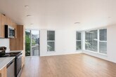 This thoughtfully designed single-floor unit offers a clean, contemporary aesthetic throughout. The open-concept living and kitchen area serves as the heart of the space, featuring warm light wood-style flooring that extends seamlessly across the main areas. Large windows flood the living space with natural light and offer views of the surrounding neighborhood, creating an airy and welcoming atmosphere.

The kitchen is outfitted with modern light wood cabinetry reaching to the ceiling, stainless steel appliances including a refrigerator, electric range, and over-the-range microwave, as well as a sleek white countertop and integrated sink — combining functionality with a fresh, contemporary look.

The bedroom is carpeted for comfort and features a large window fitted with horizontal blinds, providing both natural light and privacy. A set of sliding closet doors offers convenient built-in storage. The bathroom maintains the unit's clean design language with light wood vanity cabinetry, a white countertop, hardwood-style flooring, and a full bathtub. Throughout the unit, crisp white walls, recessed lighting, and consistent modern finishes create a cohesive and inviting living environment.