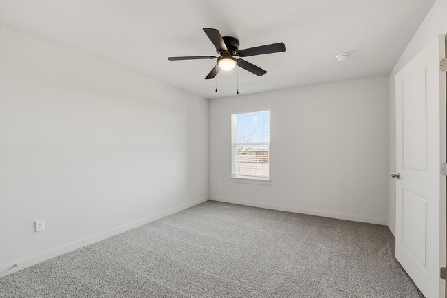 Bright and airy bedroom with plush gray carpeting, contemporary ceiling fan, and large window for natural light. - Oaks at Mustang