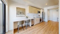 Located at 2211 S 300 W in South Salt Lake, Utah, this thoughtfully designed one-bedroom, one-bathroom unit maximizes every inch of its compact footprint. The open-plan layout seamlessly connects the kitchen, dining area, and living room, creating a cohesive and functional living space.

The kitchen is outfitted with light wood cabinetry featuring gold-toned hardware, white quartz countertops, a subway tile backsplash, and a full suite of stainless steel appliances including a range, microwave, dishwasher, and refrigerator. A built-in counter with bar seating serves as both a dining and workspace area.

The living room is bright and airy, anchored by a large floor-to-ceiling window that frames outdoor views and fills the space with natural light. Light wood-tone flooring runs throughout, adding warmth to the clean, white walls. A wall-mounted climate control unit ensures year-round comfort.

The bedroom is cozy and well-appointed, featuring soft neutral tones and warm accent lighting. The bathroom offers a clean, modern aesthetic with a frameless sliding glass shower enclosure, warm wood vanity cabinetry, and white countertops. Light wood flooring continues throughout, tying the space together with a consistent, contemporary feel.