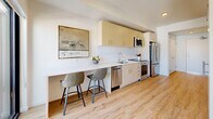 Located at 2211 S 300 W in South Salt Lake, Utah, this thoughtfully designed one-bedroom, one-bathroom unit maximizes every inch of its compact footprint. The open-plan layout seamlessly connects the kitchen, dining area, and living room, creating a cohesive and functional living space.

The kitchen is outfitted with light wood cabinetry featuring gold-toned hardware, white quartz countertops, a subway tile backsplash, and a full suite of stainless steel appliances including a range, microwave, dishwasher, and refrigerator. A built-in counter with bar seating serves as both a dining and workspace area.

The living room is bright and airy, anchored by a large floor-to-ceiling window that frames outdoor views and fills the space with natural light. Light wood-tone flooring runs throughout, adding warmth to the clean, white walls. A wall-mounted climate control unit ensures year-round comfort.

The bedroom is cozy and well-appointed, featuring soft neutral tones and warm accent lighting. The bathroom offers a clean, modern aesthetic with a frameless sliding glass shower enclosure, warm wood vanity cabinetry, and white countertops. Light wood flooring continues throughout, tying the space together with a consistent, contemporary feel.