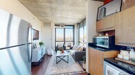 This contemporary urban residence in Denver, Colorado offers three bedrooms and three bathrooms across a well-planned single-floor layout with a distinct industrial-modern aesthetic. Exposed concrete ceilings, rich hardwood flooring, and floor-to-ceiling windows define the character of the space throughout.

The open-concept living area is anchored by expansive windows that flood the room with natural light and frame sweeping views of the Denver skyline and surrounding cityscape. The adjacent kitchen features warm wood cabinetry, dark countertops, stainless steel appliances, and a compact, efficient design that connects seamlessly to the living and dining areas.

Each of the three bedrooms carries the signature concrete ceiling detail, lending a cohesive industrial feel. The primary bedroom is generously sized and benefits from large windows with prominent city views, including a notable church steeple on the horizon. A second bedroom mirrors this view and offers ample space for both sleeping and a dedicated workspace. The third bedroom is more intimate in scale, accented by bold décor against its clean, neutral walls.

The three bathrooms are cleanly finished, with one notably featuring accessibility grab bars. Connecting hallways display a mix of concrete and drop-tile ceiling treatments. This residence delivers a compelling blend of urban style, natural light, and practical living in the heart of Denver.