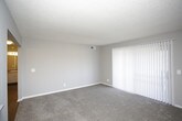 This single-floor unit is designed with a practical, straightforward layout that maximizes functionality. The kitchen is efficiently arranged in a galley configuration, featuring white cabinetry with ample upper and lower storage, a double stainless steel sink with grey laminate countertops, and white appliances including a coil-burner electric range. Wood-look vinyl plank flooring runs throughout the kitchen, adding warmth to the space.

The living area is generously proportioned, finished with neutral grey carpet and grey-toned walls. A pass-through window connects the living space to the kitchen, enhancing openness between the two areas. A sliding glass door fitted with vertical blinds allows natural light to filter in and provides access to the exterior. A separate entrance door is also present in the living area.

The bedroom offers comfortable dimensions, with plush grey carpet, a ceiling fan with integrated lighting, and a window with horizontal blinds that admits natural light. Neutral wall tones carry throughout, maintaining a cohesive, understated aesthetic.

The bathroom is clean and straightforward, featuring a full-size soaking tub with an overhead shower, chrome fixtures, and a white surround. A textured ceiling is consistent throughout the unit, adding subtle visual character to the otherwise streamlined interior.