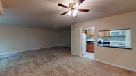 This single-floor residence offers a practical and comfortable layout spread across several distinct areas. The living room is generously sized, finished with wall-to-wall carpeting and a ceiling fan with integrated lighting, creating a functional and comfortable gathering space. Large windows along one wall allow natural light to filter in and provide pleasant views of surrounding greenery, enhancing the room's open, airy feel.

The kitchen is accessed through a dedicated doorway and is well-appointed with warm oak cabinetry offering ample upper and lower storage, dark speckled countertops, a stainless steel sink, and a full suite of white appliances including a refrigerator, dishwasher, and range. The tile flooring in the kitchen contrasts with the carpeting throughout the rest of the unit.

The bedroom provides a comfortable retreat with carpeted flooring, a built-in closet with bifold doors offering substantial storage, and access to additional rooms. A full bathroom serves the space, featuring an oak vanity with a white countertop and sink, a framed mirror, and a shower-tub combination. The neutral color palette throughout the residence contributes to a clean, cohesive aesthetic.