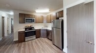 Located at 875 21st Ave SE in Rochester, Minnesota, this single-floor unit offers a practical and well-appointed layout designed for comfortable everyday living. The open living area features a combination of durable hardwood-style flooring and plush carpeting, with a ceiling fan overhead and a large window that allows natural light to fill the space. Baseboard heating is present throughout, ensuring consistent warmth across all rooms. The kitchen is equipped with a full suite of stainless steel appliances, including a refrigerator, electric range, built-in microwave, and dishwasher. Rich dark-toned cabinetry pairs with light stone-finish countertops, and the hardwood-style flooring continues seamlessly through this space. The bedrooms are carpeted for comfort, each featuring wide windows with exterior views, baseboard heating, and ceiling fans where applicable. Sliding panel doors provide closet access in the bedrooms. The bathroom is well-finished with a granite-style vanity countertop, dark wood wall cabinetry for additional storage, a full tub-shower combination, and wood-look flooring. Textured ceilings are consistent throughout the unit, contributing to its cohesive, understated aesthetic. The overall design is clean, neutral, and move-in ready.