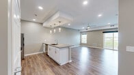 Located at 2400 N Forest Rd in Getzville, NY, this well-appointed one-bedroom, one-bathroom residence offers a thoughtfully designed single-floor layout with modern finishes throughout. The open-concept kitchen and living area serves as the heart of the home, featuring a large center island with granite countertops, undermount sink, and elegant pendant lighting. White shaker-style cabinetry pairs seamlessly with stainless steel appliances, including a gas range, microwave, and refrigerator. Recessed lighting and a striking coffered ceiling detail add architectural interest to the space. Durable hardwood-style flooring extends throughout the main living areas, while the living room benefits from a ceiling fan and a sliding glass door that opens to a private outdoor balcony, filling the space with natural light. The spacious bedroom is finished with plush carpet, a large window with outdoor views, and direct access to a walk-in closet. The full bathroom features white cabinetry, granite countertops, a full vanity mirror, and a tall linen storage cabinet. Additional conveniences include two closets, an in-unit laundry area, and a clean, neutral color palette that gives the space a bright and welcoming ambiance throughout.